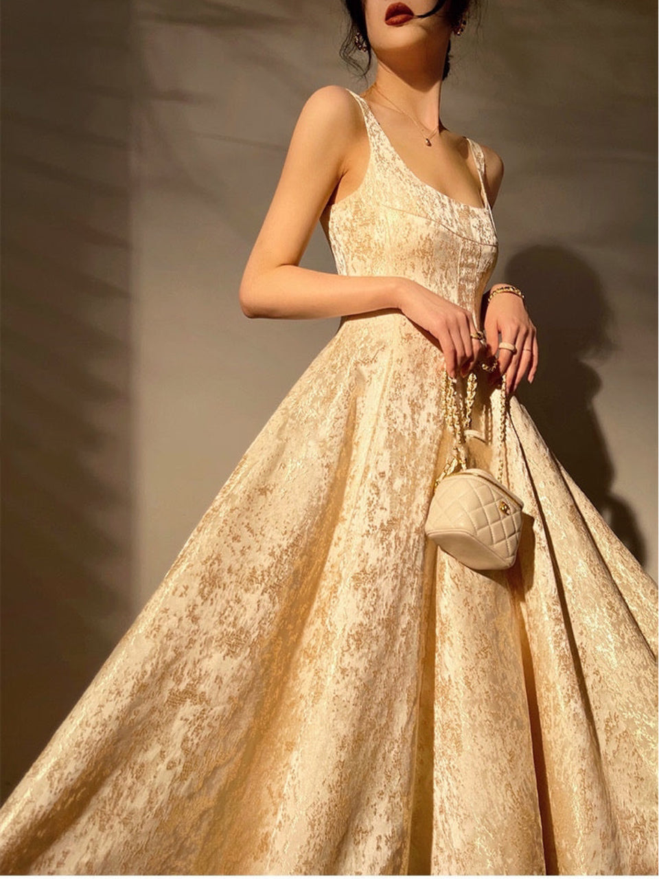 A model wearing a sleeveless, high-waisted, gold jacquard fabric evening dress with a U-shaped neckline and a voluminous skirt.