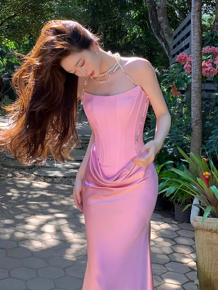 A person wearing a pink sleeveless dress with a fitted waist and a flowing skirt, standing outdoors.