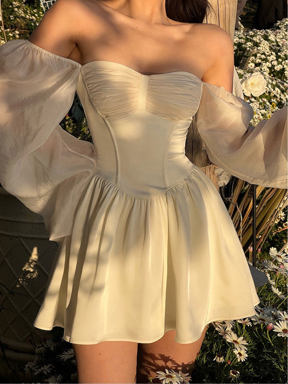 A woman wearing an off-white, short A-line dress with a pleated bodice, puff sleeves, and a sweet heart neckline.