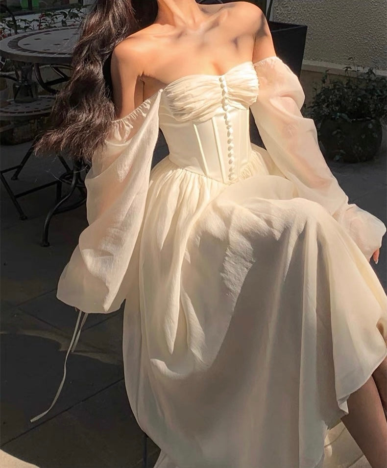 Woman wearing a white strapless dress with sheer sleeves in an outdoor setting.