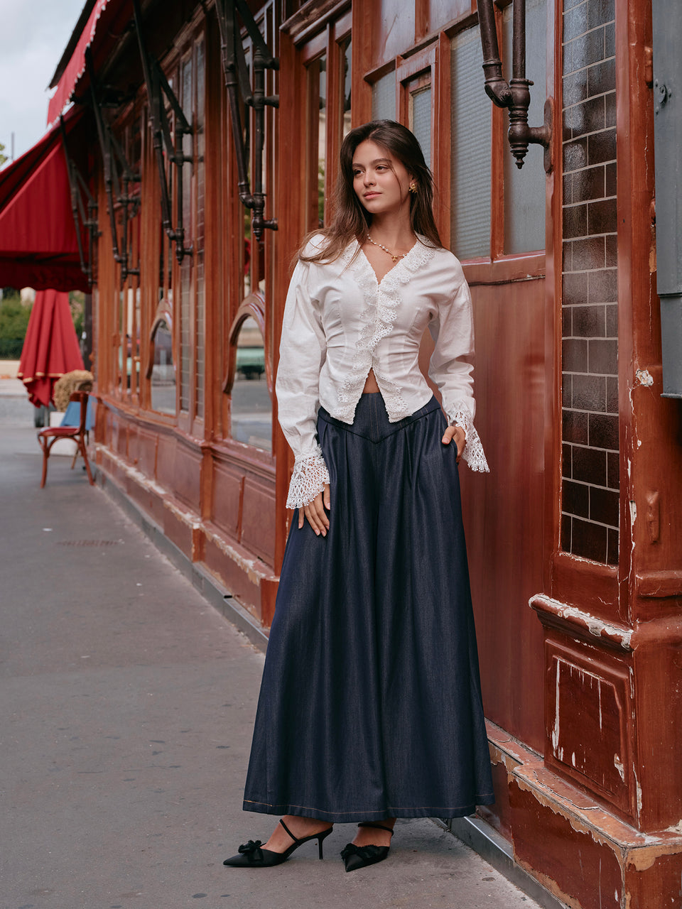 Woman in a white blouse and dark blue skirt standing on a street with a building in the background.